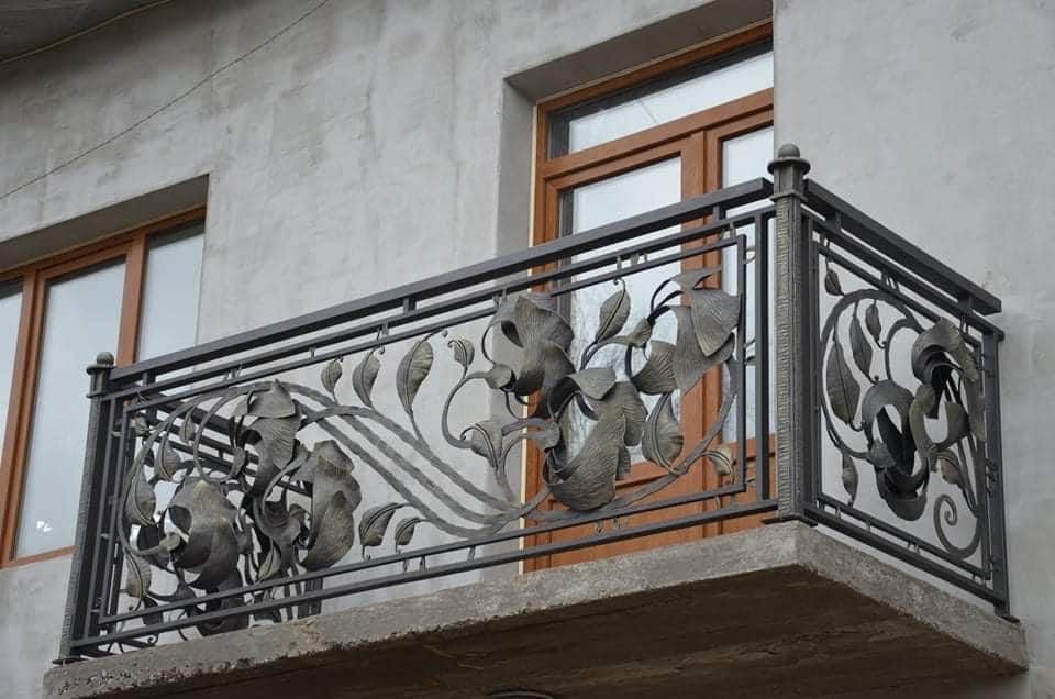 Masywna, kuta balustrada balkonowa ze stali malowanej proszkowo z ozdobnymi elementami kwiatowymi.