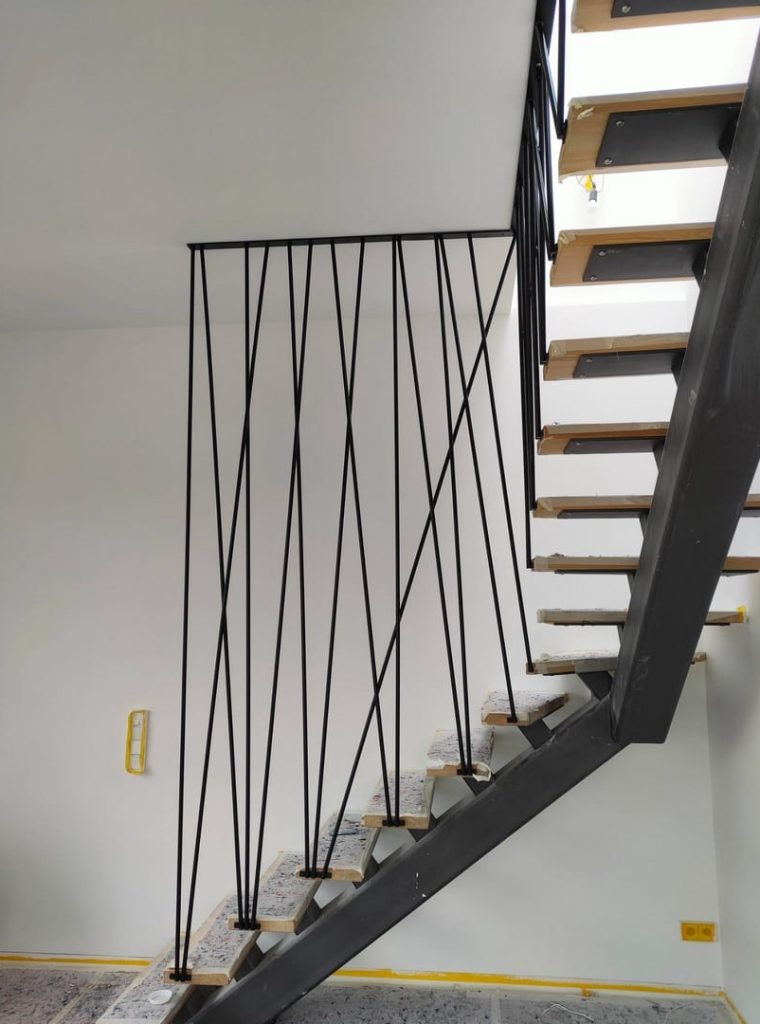 Eine von MetalWork Poland auf Bestellung gefertigte Innentreppe. Die Konstruktion der Treppe aus schlanken, graphitfarbenen Metallstäben schafft eine dynamische, aber leichte Form. Die Stufen aus Holz in einem warmen Farbton ergänzen das Ganze perfekt. Die Treppe wurde perfekt an den Raum des modernen, hellen Interieurs des Hauses angepasst und bildet mit ihm eine kohärente, stilvolle Komposition. Sie sind ein funktionelles und ästhetisch ansprechendes dekoratives Element dieser Einrichtung.